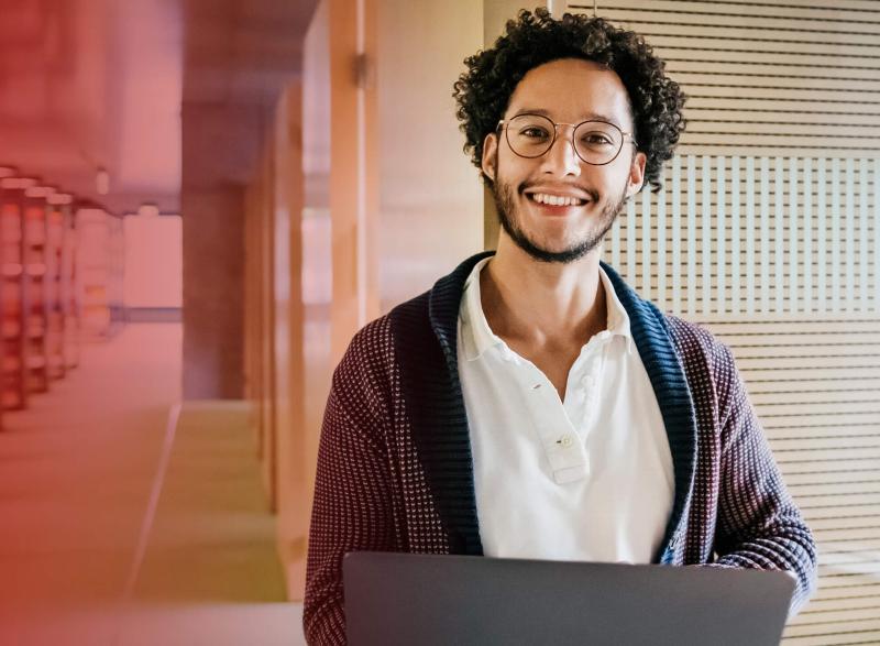 Bild eines Studenten der Knappschaftlichen Sozialversicherung der mit Laptop in der Hand lächelnd zum Betrachter schaut